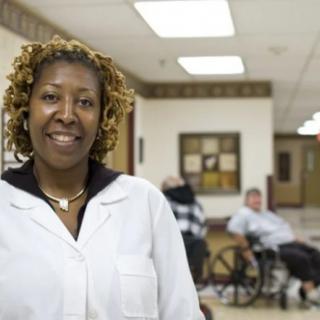 A healthcare professional smiling in a hospital hallway with patients in the background.