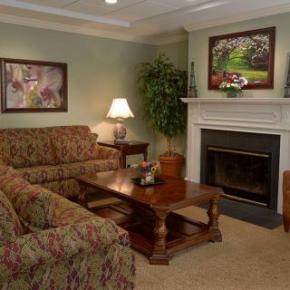 A cozy living room with a sofa, coffee table, and fireplace, decorated with paintings and plants.