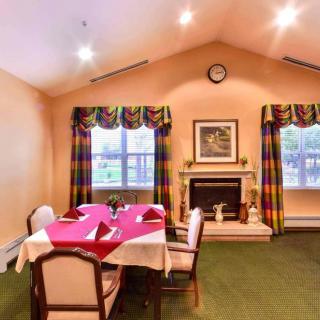 A cozy dining room with a table set for guests, featuring a fireplace and large windows with colorful curtains.
