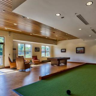 A spacious lounge featuring a pool table, green carpet, and comfortable seating near large windows.