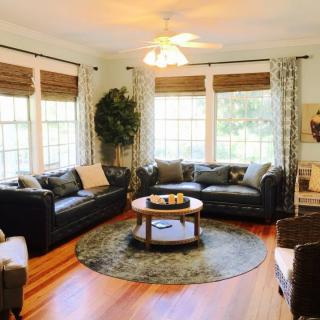 A cozy living room with ample natural light, featuring leather sofas and a central coffee table.