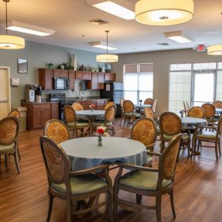 A spacious dining room with multiple tables and chairs, featuring modern lighting and a small kitchen area.