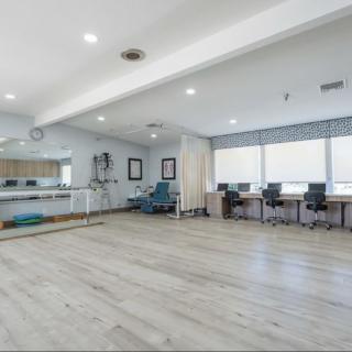 A spacious office area with desks and chairs, well-lit by natural light from large windows.