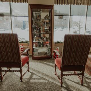 A cozy living room setup featuring two vintage chairs and a display cabinet by a large window.