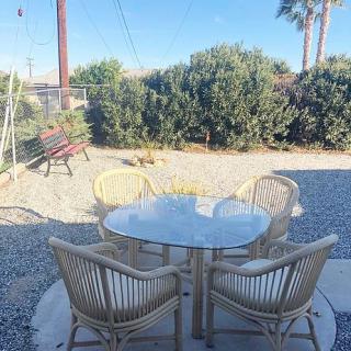 A cozy outdoor patio area with a glass table and chairs surrounded by greenery.