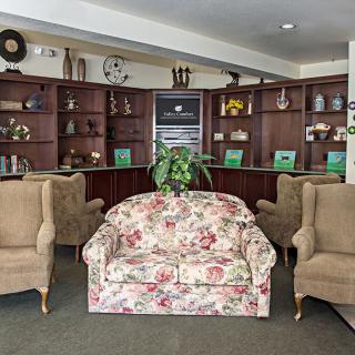 A cozy living room with a floral sofa, beige armchairs, and a wooden bookshelf in the background.