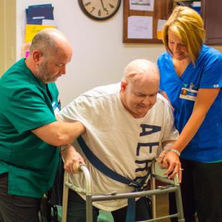 Healthcare workers assist an elderly man using a walker during rehabilitation.