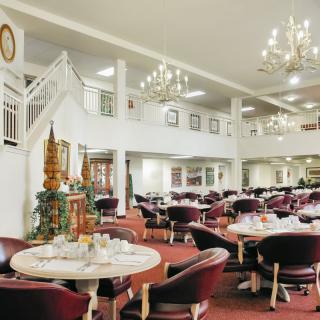 An elegant dining area with multiple tables and chairs, illuminated by chandeliers.