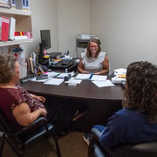 A group discussion in an office setting, with individuals seated around a desk.