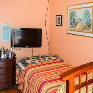 A cozy bedroom with a single bed, a wall-mounted television, and a wooden dresser.