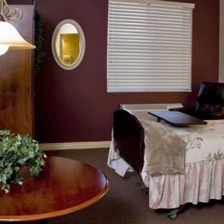 A cozy bedroom with a bed, oval mirror, window blinds, and a small table with a plant.