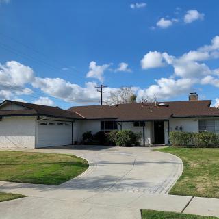 A suburban house with a large driveway and front yard under a partly cloudy sky.