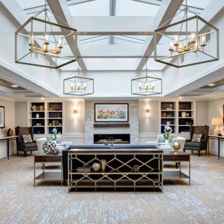 A luxurious living room with elegant chandeliers, a central fireplace, and inviting seating under a skylight.