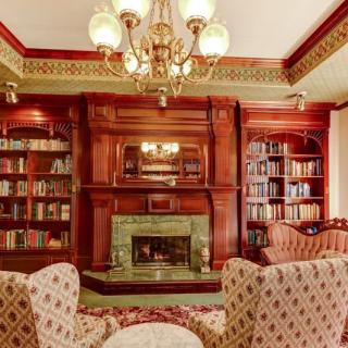 A traditional library with wooden bookshelves, a fireplace, and elegant armchairs.