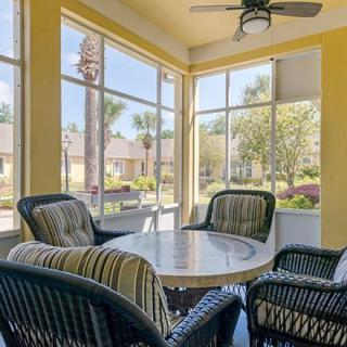 A bright sunroom with wicker furniture and large windows offering a view of the outdoors.