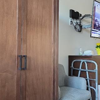 A glimpse of a hospital room featuring a wardrobe, a chair, and a wall-mounted television.