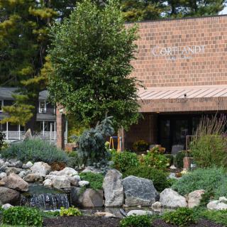 A scenic view of a building surrounded by a well-maintained garden with rocks, trees, and a small water feature.