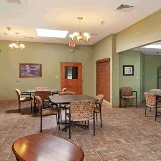 A spacious dining area with multiple tables and chairs set against green walls, featuring elegant lighting fixtures.