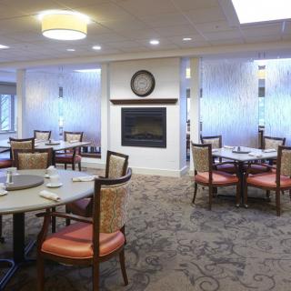 A cozy dining room with multiple tables and chairs, featuring a central fireplace.