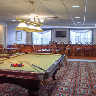 A well-lit game room featuring a pool table, chairs, and a television.