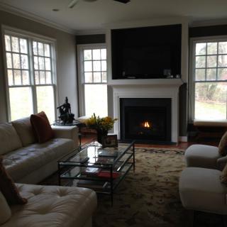 A cozy living room with a fireplace, featuring a comfortable sofa, large windows, and a sleek coffee table.