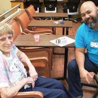 An elderly woman enjoys a moment with a caregiver, sharing smiles and conversation in a cozy indoor setting.