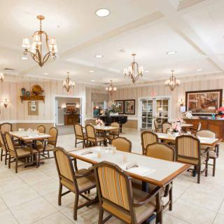 A well-lit restaurant dining area with neatly arranged tables and chairs, featuring elegant chandeliers and tasteful decor.