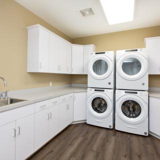 A modern laundry room featuring four stacked washers and dryers, with ample white cabinetry and counter space.