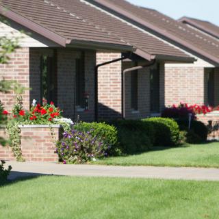 A row of suburban brick houses with well-maintained lawns and flowerbeds.