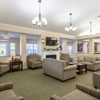 A cozy and well-lit living room with multiple seating arrangements centered around a fireplace, featuring sofas, armchairs, a coffee table, and overhead chandeliers.
