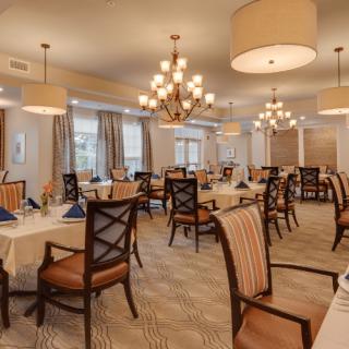 An elegant dining room with neatly arranged tables and chairs, illuminated by chandeliers.