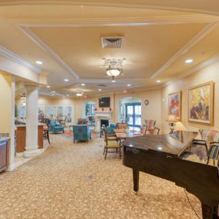 A spacious and well-lit lounge featuring a piano, artwork on the walls, and comfortable seating areas.