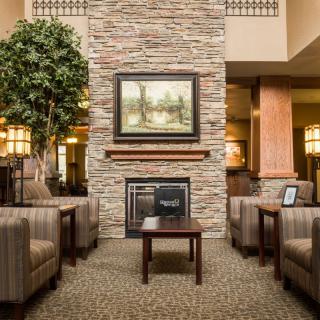 A cozy hotel lobby features comfortable seating and a central fireplace, surrounded by elegant decor.