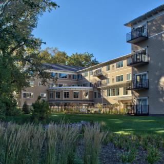 A residential apartment building with balconies surrounded by greenery on a sunny day.