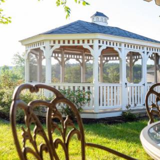 A charming white gazebo in a sunlit garden, surrounded by outdoor furniture.