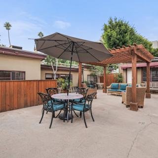 A spacious outdoor patio featuring a dining set with an umbrella and comfortable seating under a pergola.
