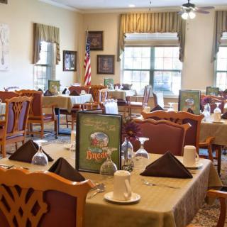 A well-arranged dining area featuring neatly set tables, chairs, and windows allowing natural light.