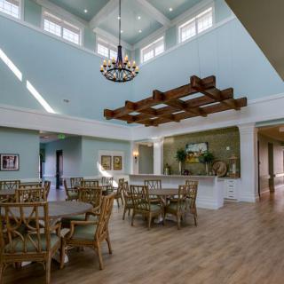 A spacious dining area with high ceilings, featuring a chandelier and wooden furniture, illuminated by natural light.