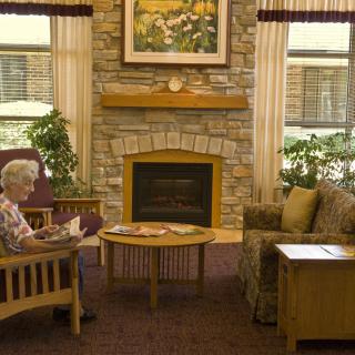 An elderly person sitting and reading in a cozy living room with a fireplace.