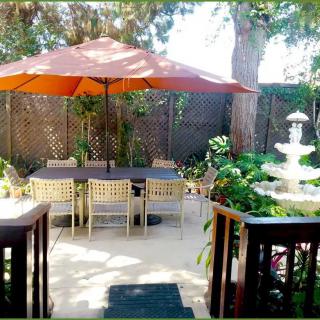 An inviting outdoor patio with a dining set under a large umbrella, surrounded by lush greenery and a decorative fountain.