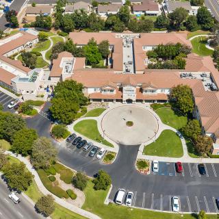 Aerial view of a building complex with surrounding greenery and a parking lot.