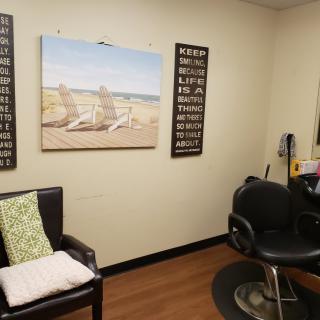 A cozy hair salon interior with a comfortable styling chair, wall art, and decorative cushions.