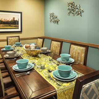 A dining room with an elegant table setting featuring blue dishes and a yellow table runner, complemented by wall art and a photograph.