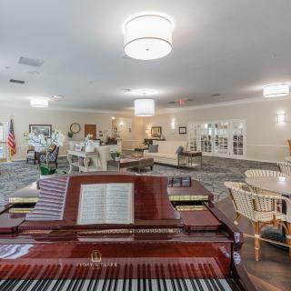 A spacious lounge area featuring a grand piano and ample seating, illuminated by stylish chandeliers.