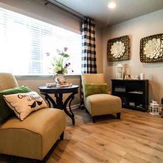 A cozy living room with two beige chairs, green accents, and a wooden floor.