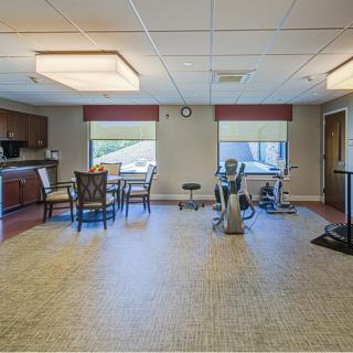 A spacious room with exercise equipment, tables, and chairs, featuring large windows and ample lighting.