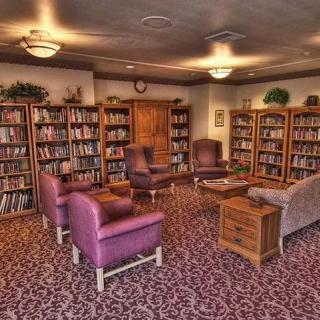 A cozy library reading room with bookshelves, armchairs, and a patterned carpet.