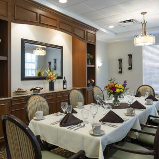 An elegantly set dining room with a neatly arranged table, featuring flowers and fine dining settings.