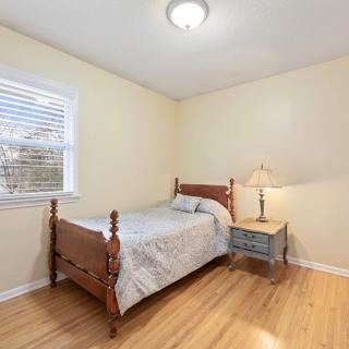 A simple bedroom featuring a single bed, a lamp on a nightstand, and a window with blinds.