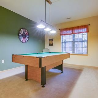 A cozy game room featuring a billiards table, a large wall clock, ambient lighting, and a window with natural light.